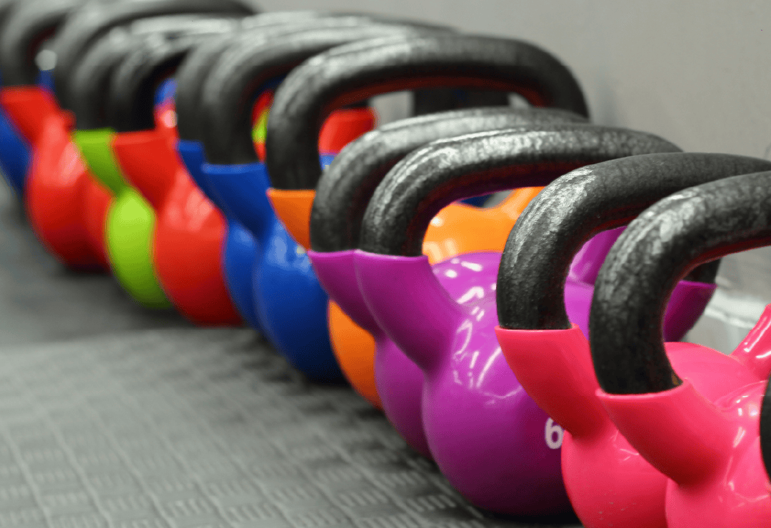 Kettlebells in various colors arranged on a gym floor, ready for workout sessions.