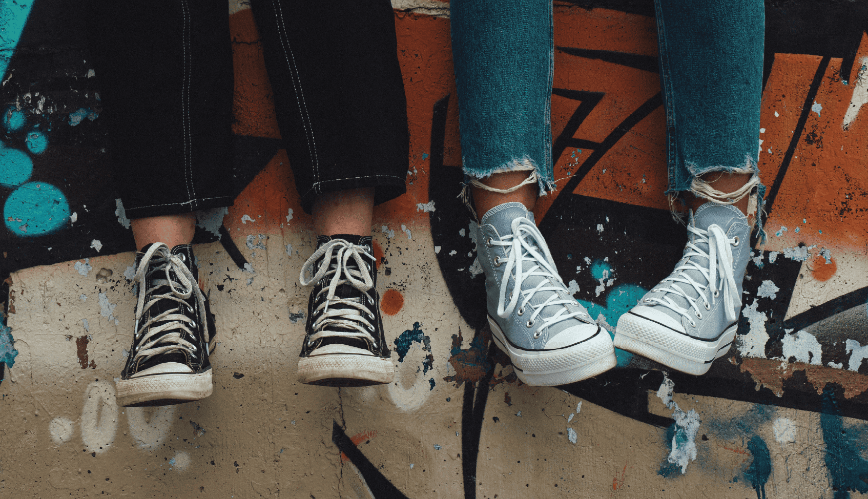 Two children sitting on a graffiti-covered ledge, wearing sneakers.